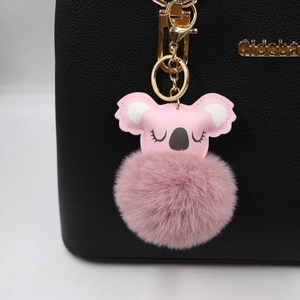 Pink plush koala ball keychain with golden metal clasp on black leather bag