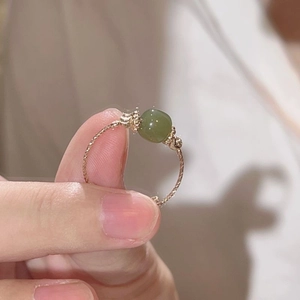 Vintage style gold rope ring with a translucent green bead shown on a woman's finger