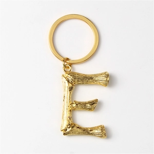 Detailed close-up of golden metal letter E keychain with bamboo texture design