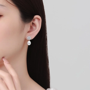 Elegant white pearl drop earrings with silver flower stud worn by model on grey background