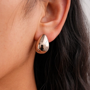 Close-up of polished silver teardrop earrings worn by a model with long dark hair
