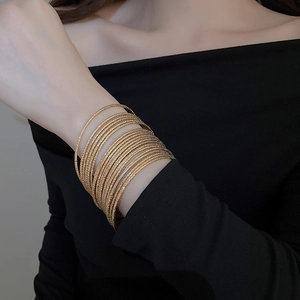 Close-up of a 20-piece set of thin gold metal bangles with textured finish on a model