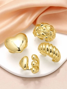 Detail of four gold-plated heart and geometric textured open rings on silk fabric