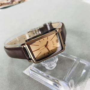 Macro detail of rose gold rectangular watch case and textured brown leather strap