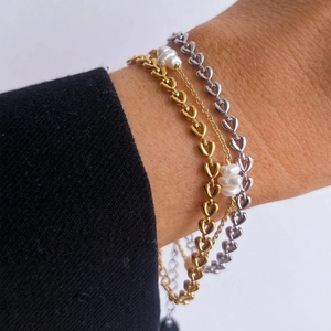 Dettaglio di braccialetti a catena con cuore e perle d'acqua dolce su un polso
