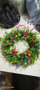 Close-up of colorful artificial flower wreath with green leaves on dry branch base