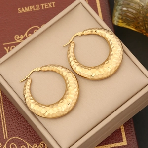Detailed macro of thick gold-plated stainless steel hoop earrings with hammered texture
