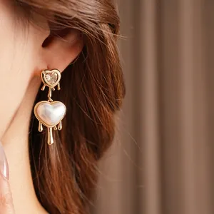 Elegant gold heart earrings with zircon and pearl tassels shown on a model