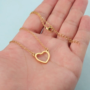 Minimalist gold hollow heart pendant necklace in stainless steel held against blue background