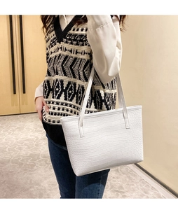 Detail shot of white crocodile pattern tote bag held by a model in a minimalist room
