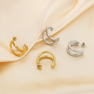 Detail of gold and silver double-layered C-shaped earrings on elegant champagne silk fabric