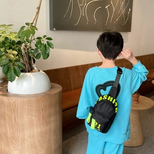 Sacoche bandoulière noire enfant avec lettres fluo portée par un garçon stylé en bleu