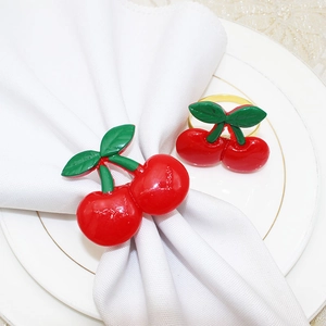 Detailed view of red cherry napkin rings with green leaves on white linen and a ceramic plate