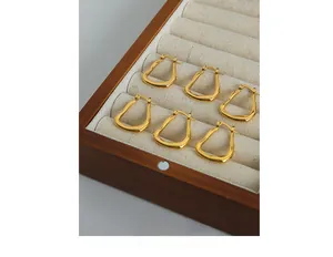 Three pairs of irregular U-shaped gold plated geometric hoop earrings in a wooden jewelry box