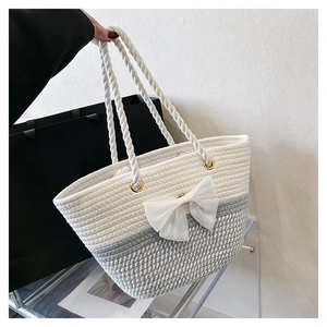 Detail of hand-woven tote bag featuring a white lace bow and rope handles close-up