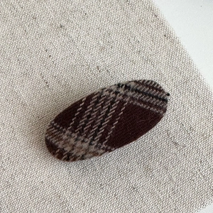 Detail of oval hair clip with brown and beige checkered wool fabric on linen background