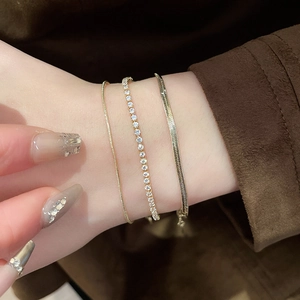 Close-up of a three-piece gold snake chain and zircon tennis bracelet set on wrist