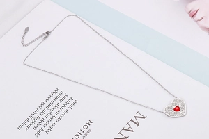 Close-up of silver heart pendant with red gem and pavé crystals on a minimalist chain