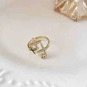 Dettaglio dell'anello aperto dorato con design a doppia stella in zircone e gemma lucida
