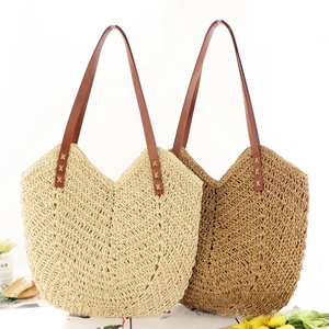 Detail of hand-woven straw tote bag showing hollow V-pattern texture and leather straps
