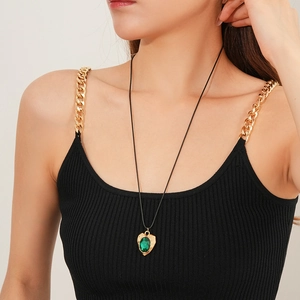 Close-up of a vintage gold heart necklace with a green oval gemstone on a black cord