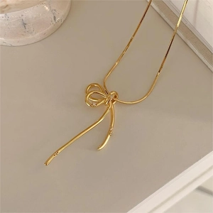 Detail of gold-plated snake chain necklace featuring a crystal-studded bow pendant