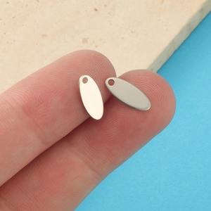 Close-up of polished stainless steel oval charms held between fingers for DIY jewelry making