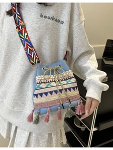 Ethnic style blue bucket bag with colorful fringes and woven shoulder strap on model