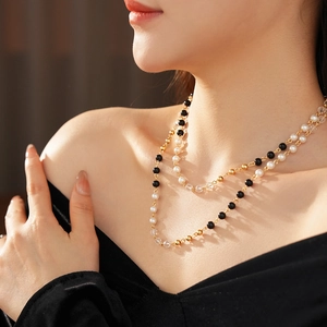 Détail d'un collier double épaisseur avec perles blanches, perles noires et chaîne dorée