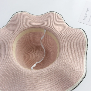 Detail of pink straw sun hat with wavy black and white brim and adjustable wind rope
