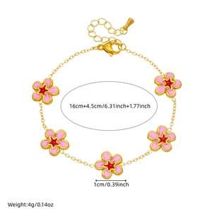 Gold chain bracelet with five pink enamel flowers and red star details on white backdrop
