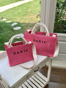 Detail of pink straw tote bags with Paris print and white fabric handles for summer beach