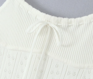 Vue détaillée du tricot blanc avec motif ajouré délicat et décoration de nœud papillon