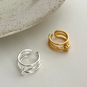 Detailed view of layered knotted 925 silver rings in gold and silver on cream background
