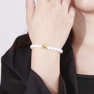 Detail of a pearl bracelet with a golden cat charm worn on a woman's wrist