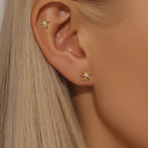 Close-up of gold flower earrings with crystals worn on earlobe and cartilage