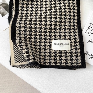 Close-up of houndstooth knit scarf texture with stitched label on a minimalist background