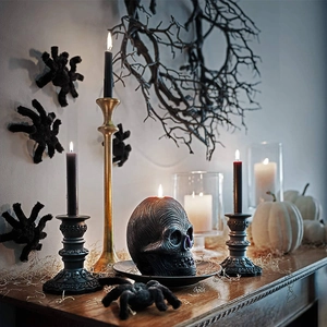 Gothic Halloween mantle setup with black skull ornament and lit candles on dark holders