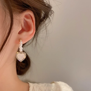 Close-up of golden heart earrings with faux pearls and rhinestones on a female model