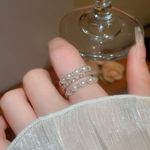 Close-up of gold layered ring with pearls and pavé diamonds worn on a female hand