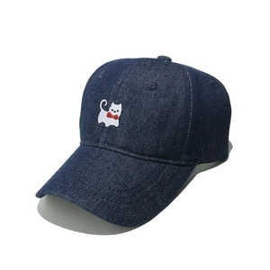 Detail of white cat embroidery with red bow on a navy blue denim baseball cap