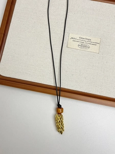 Detail view of golden wheat stalk pendant with amber bead on black cord necklace