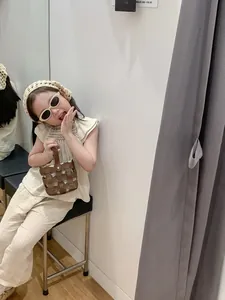 Detail of child wearing a beige linen outfit with a brown woven leather handbag