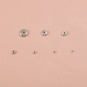 Flat round stainless steel spacer beads for DIY jewelry making in various sizes on pink fabric