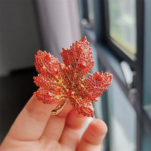 Macro detail of luxury maple leaf brooch with red crystals and gold-tone finish