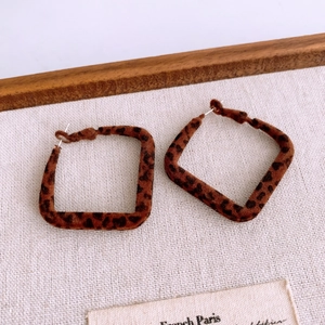 Detailed close-up of square leopard print earrings with a soft velvet texture on beige fabric
