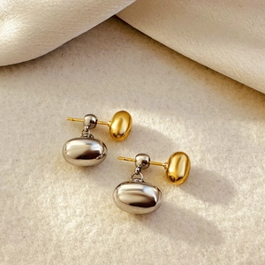 Two-tone pebble shape stud earrings in gold and silver finish on white fabric