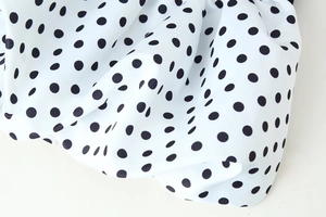 Detailed close-up of white fabric with black polka dots and smooth pleated texture