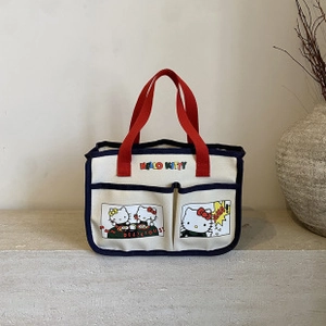 Detail of canvas tote bag showing red handles, navy trim and cartoon character pockets