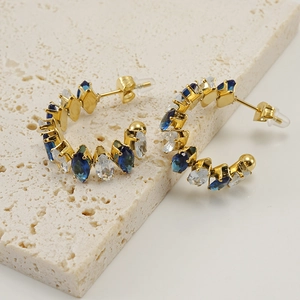 Detalle de pendientes de oro de 18K en forma de C con circonitas marquise azules